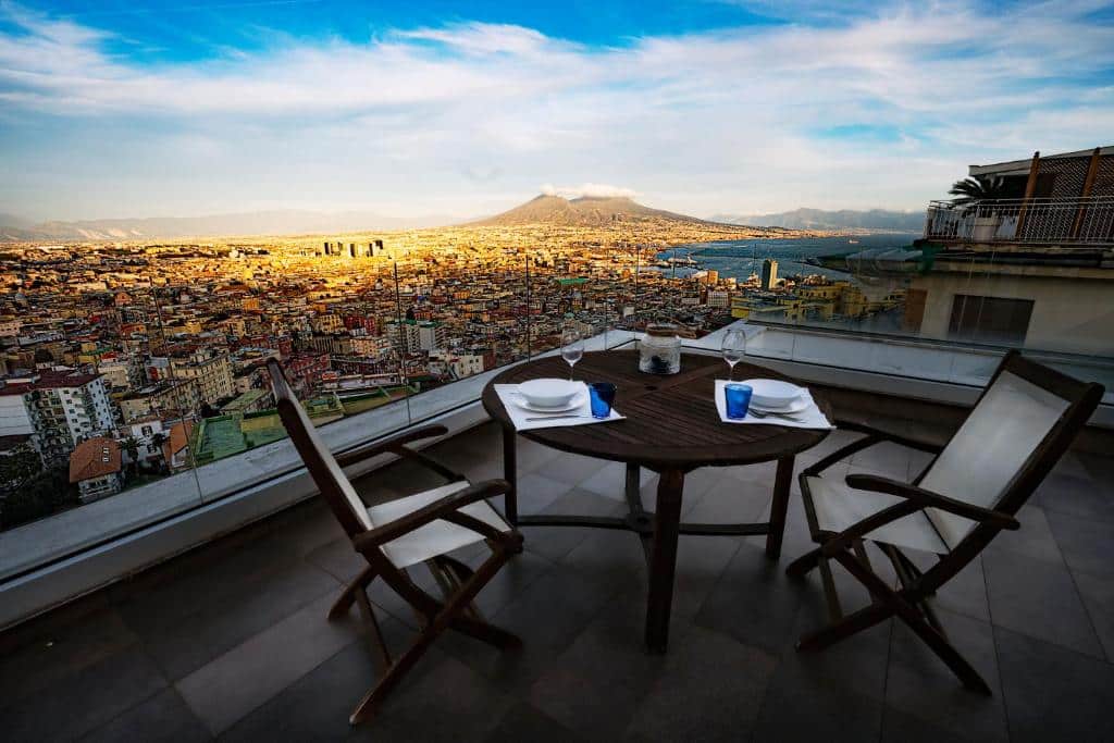 Panorama de Nápoles com o Monte Vesúvio ao fundo, visto de uma varanda com mobiliário de jardim moderno, no Terrazza Manù.
