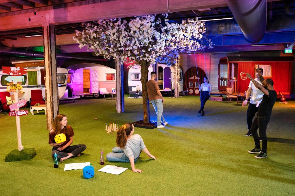 Interior do hostel Outside Inn, em Amesterdão, com uma zona de lazer de relva artificial, pessoas a conviver e caravanas retro em redor