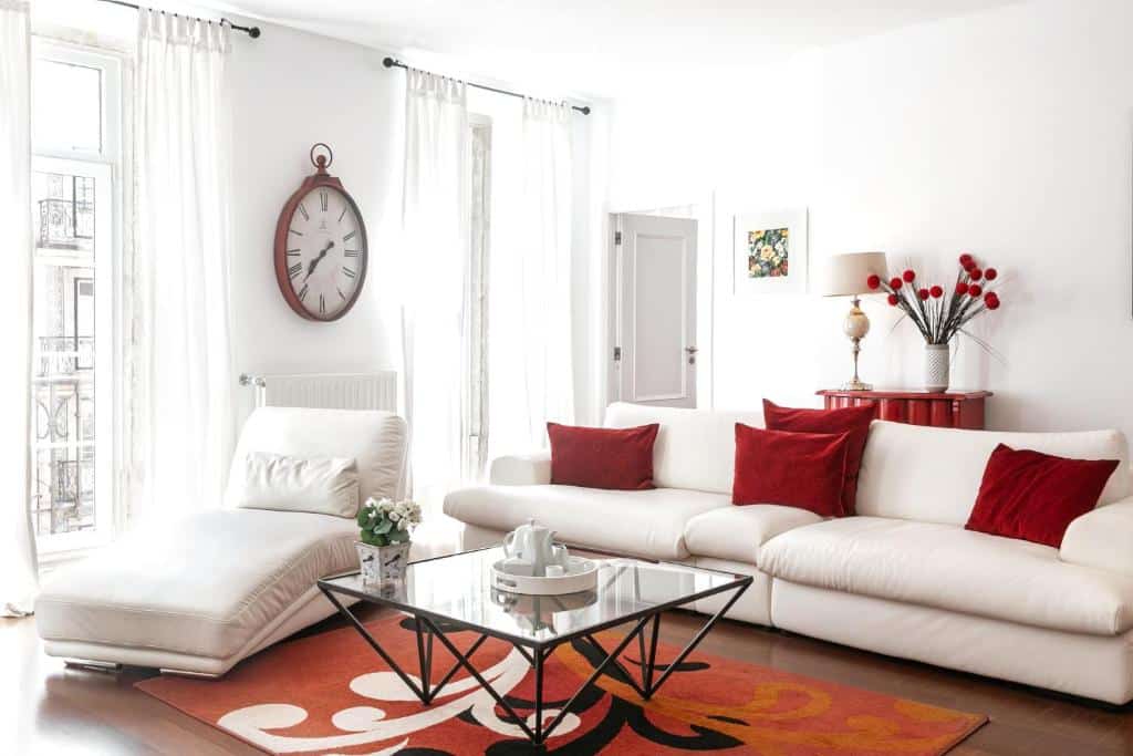 Sala de estar do Lisbon Rentals Chiado em tons de vermelho e branco, com um sofá com almofadas, duas varandas com cortinas, uma poltrona e uma mesa de centro de vidro