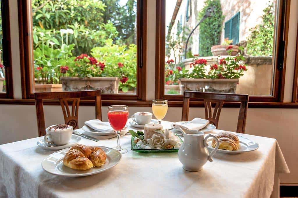 Pequeno-almoço com croissant, sumo de laranja e cappuccino em mesa posta com vista para jardim florido