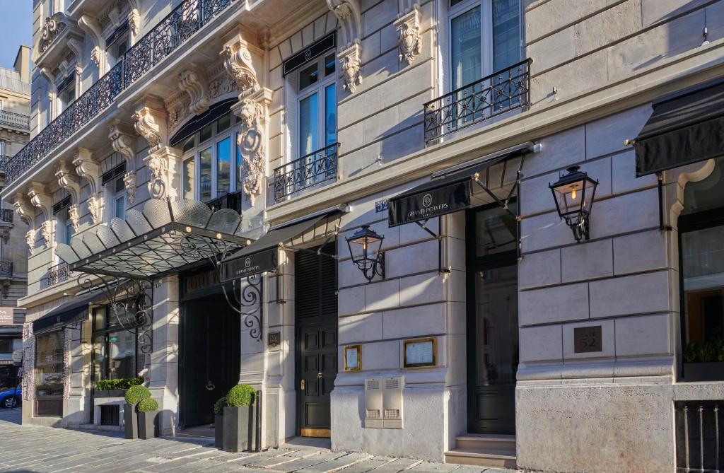Fachada de pedra de um edifício elegante, o Grand Powers Hotel, com detalhes ornamentados, janelas grandes e uma pala de vidro sobre a entrada. Este é um dos hotéis de luxo em Paris.