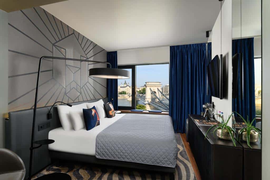 Quarto do Hotel Clark com uma cama grande, cortinas azuis, janela com vista para a cidade, arte na parede e uma cómoda com plantas e amenidades.