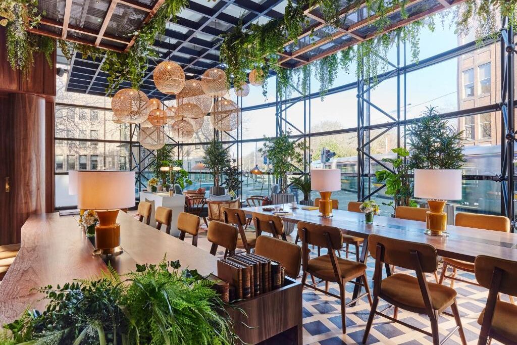 Sala de refeições no The Green com plantas suspensas, iluminação de design e cadeiras de madeira num cenário elegante.