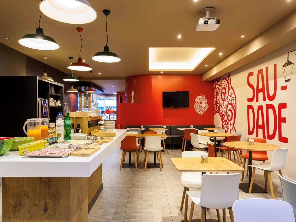 Área do pequeno-almoço do Ibis Lisboa Liberdade com mesas de madeira, cadeiras coloridas e paredes decoradas em branco e vermelho