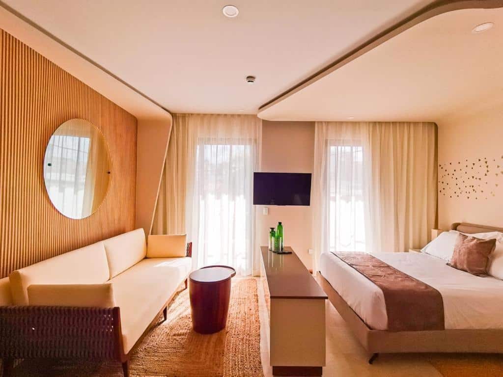 Quarto do Alizee Tower com cama de casal, sofá bege e decoração em tons terrosos.