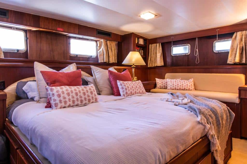 Quarto do Hotel Yacht Our Alissal com decoração em madeira, cama king size com fronhas em tons de rosa, almofadas decorativas e colcha sobre a cama.