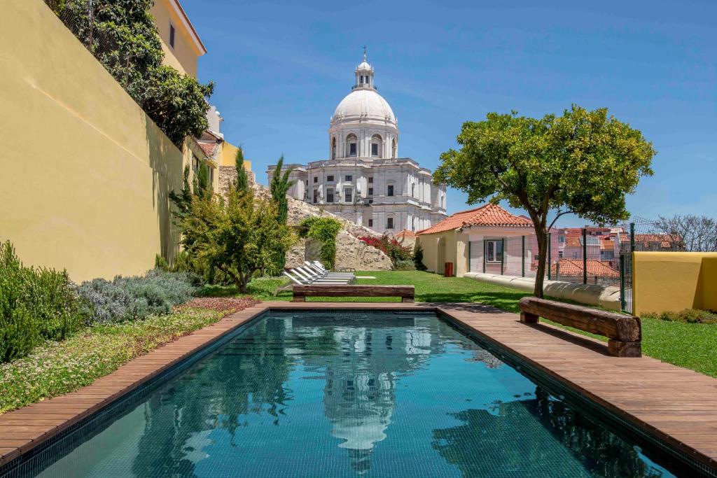 Piscina com deck e relvado com muito verde em redor, na zona exterior do Tandem Palacio Alfama Suites