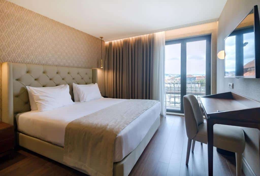 Quarto do Oca Oriental Porto Hotel com cama de casal e, em frente, uma secretária com TV na parede.