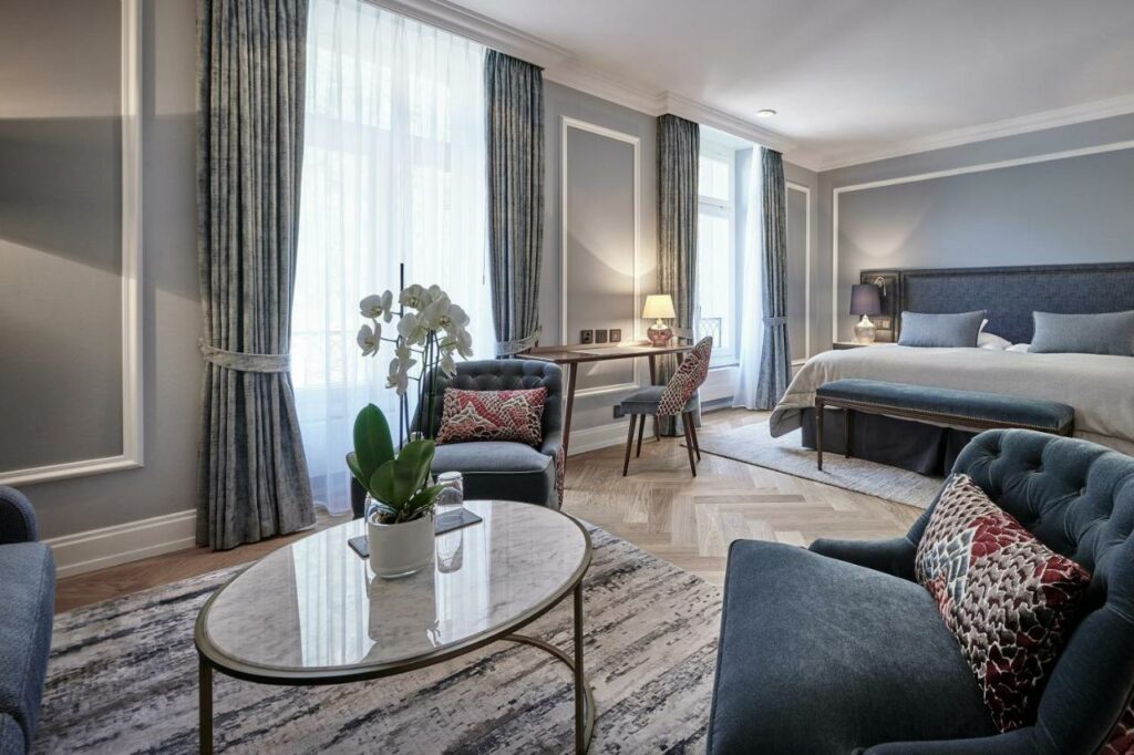 Quarto do Victoria Jungfrau Grand Hotel & Spa, com zona de estar, mesa redonda ao centro e cama de casal ao fundo.