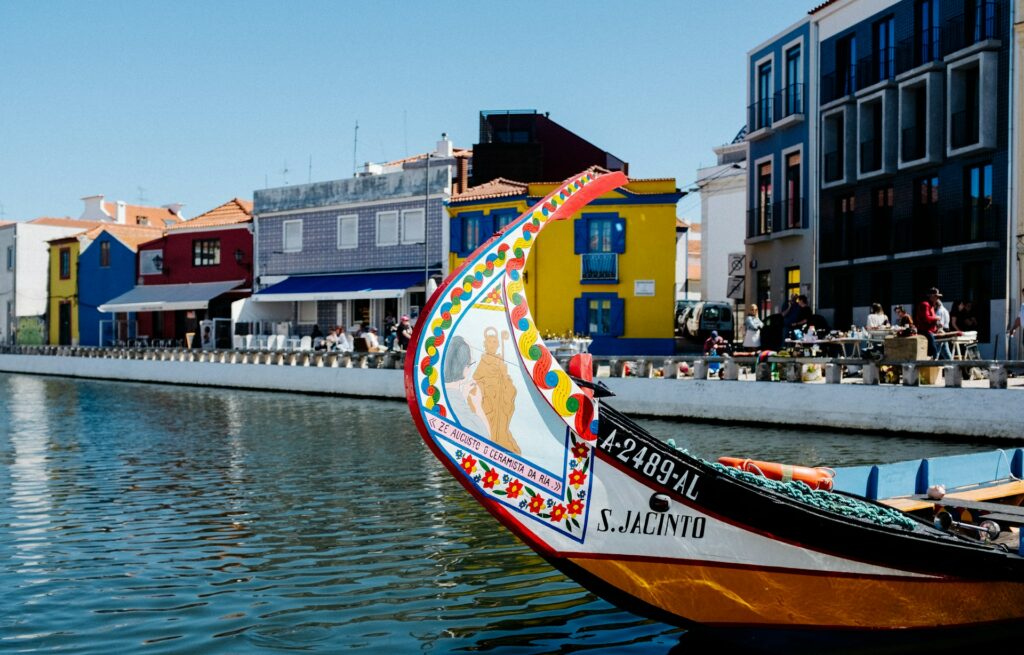 Vista de um moliceiro, barco típico com pinturas, num canal de Aveiro, com casinhas coloridas ao fundo.