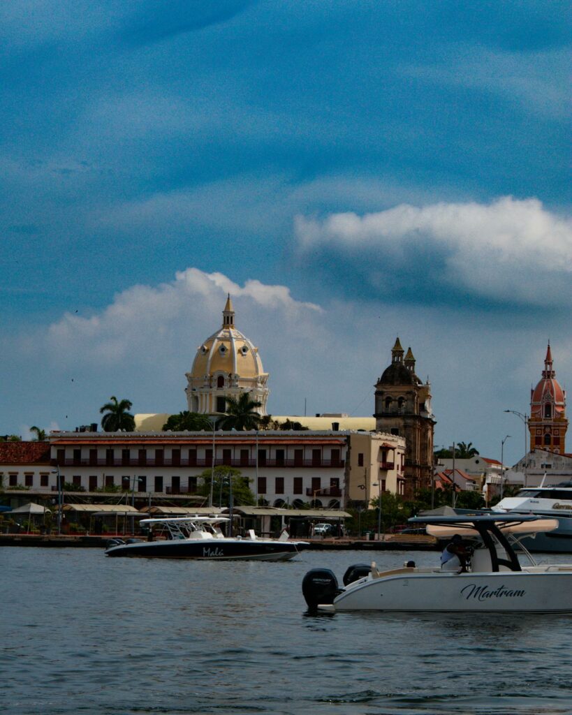 Vista a partir do mar do centro histórico de Cartagena, com barcos ancorados e as cúpulas e torres das igrejas coloniais ao fundo.