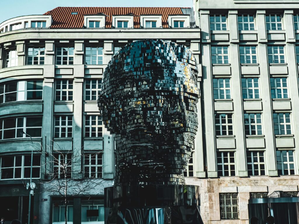 Uma escultura metálica de uma cabeça humana em frente a um edifício alto e cinzento com muitas janelas.