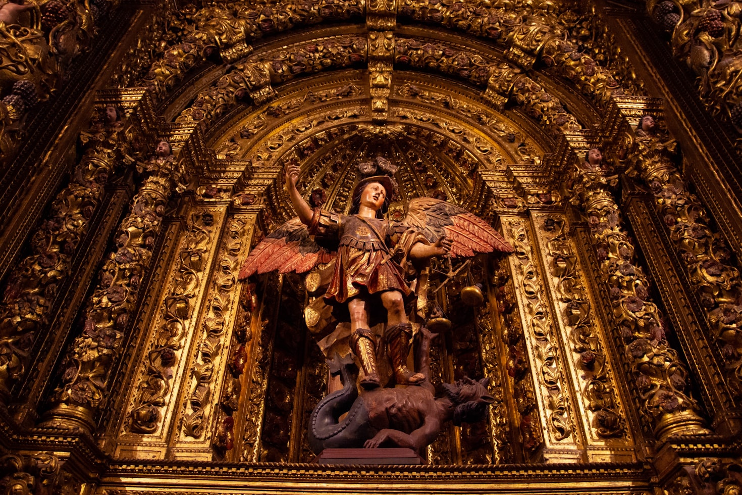 Altar religioso dourado e ornamentado, com uma estátua central de uma figura alada, na Sé do Funchal.