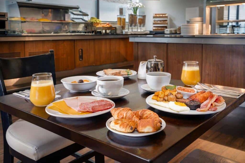Buffet de pequeno-almoço do Academy Plaza Hotel com variedade de alimentos, como croissants, fruta, iogurte, sumo de laranja e pratos quentes.