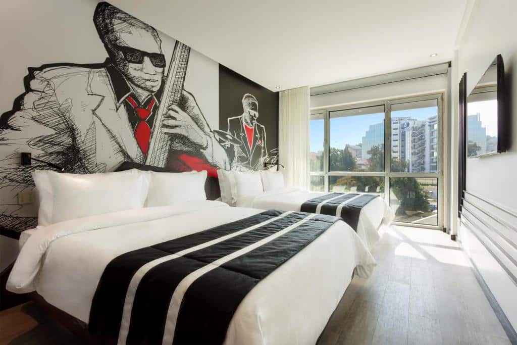 Quarto espaçoso do HF Fénix Music com duas camas de casal, uma varanda panorâmica com cortinas e, em frente às camas, uma televisão