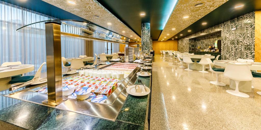 Buffet self-service moderno com produtos lácteos e zona de estar com cadeiras brancas e paredes estampadas, no Aurea Fátima Hotel Congress & Spa.