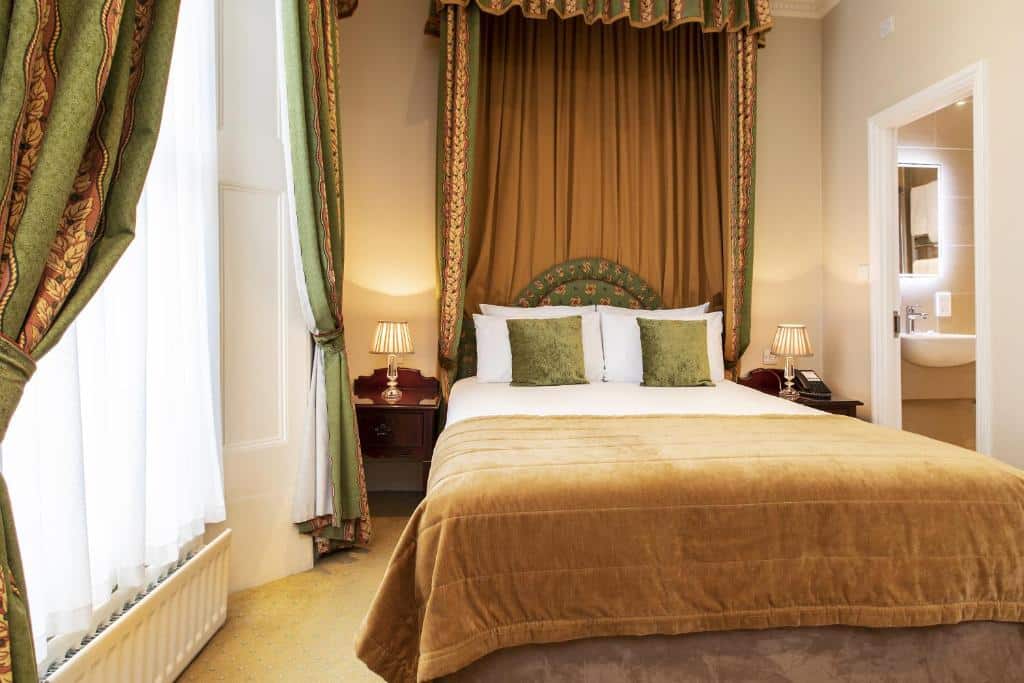 Quarto do The Windermere Hotel, London com cama de casal, cabeceira até ao teto em tons de castanho e verde, janela com cortinas e mesas de cabeceira com candeeiros