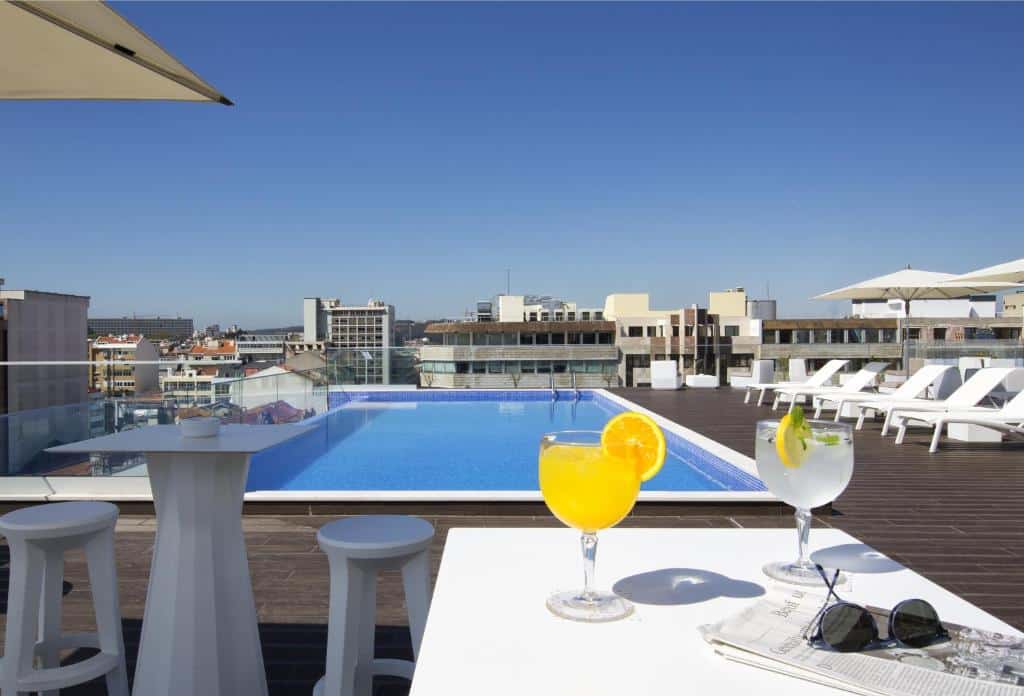Piscina na cobertura do Jupiter Lisboa Hotel, com deck espaçoso, espreguiçadeiras brancas e guarda-sóis.