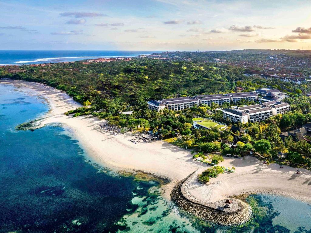 Vista aérea de um resort à beira-mar em Nusa Dua, com vegetação, praia de areia e água azul-turquesa, em Bali.