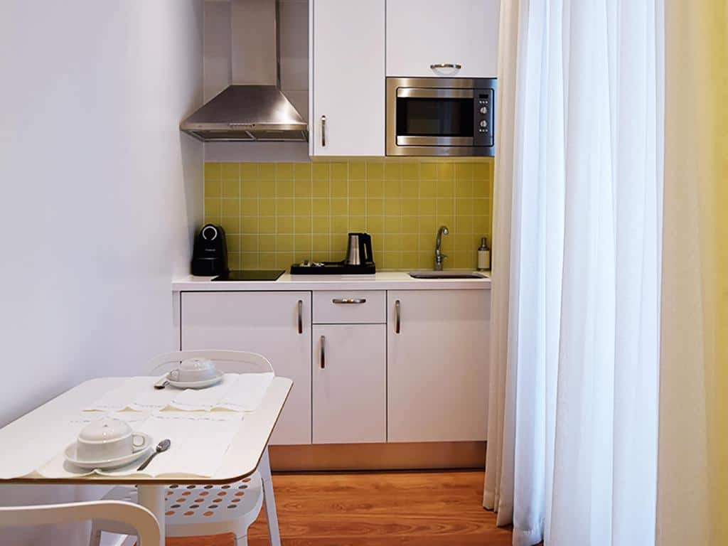 Cozinha compacta do Dream Chiado Apartments com uma janela do lado direito, alguns armários, eletrodomésticos e uma pequena mesa com duas cadeiras