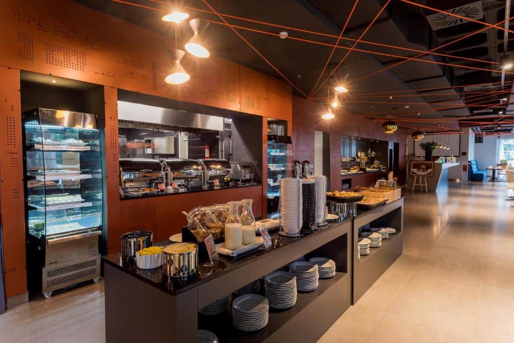 Buffet num restaurante do Star Inn Lisbon Airport, com recipientes de manter quente, pratos e cestos de pão num balcão central