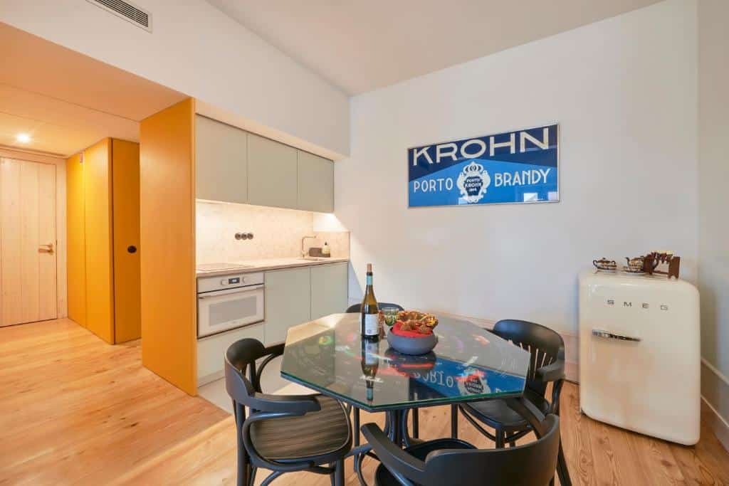 Cozinha do Cais Urban Lodge com uma mesa de vidro com quatro lugares, um pequeno frigorífico retro, alguns armários, forno e lava-loiça