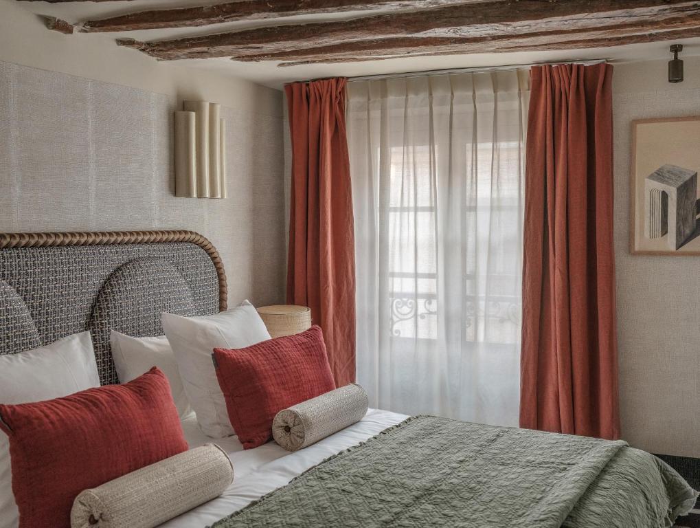Cama do Hotel Sookie com almofadas vermelhas e colcha verde, junto a uma janela com cortinas transparentes.
