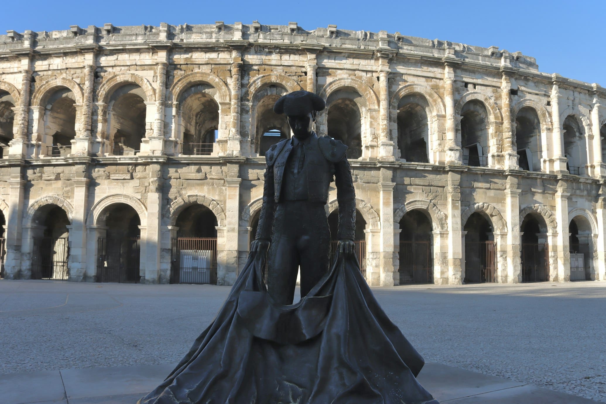 Estátua de bronze de um toureiro diante dos antigos arcos de pedra do anfiteatro romano de Nîmes.
