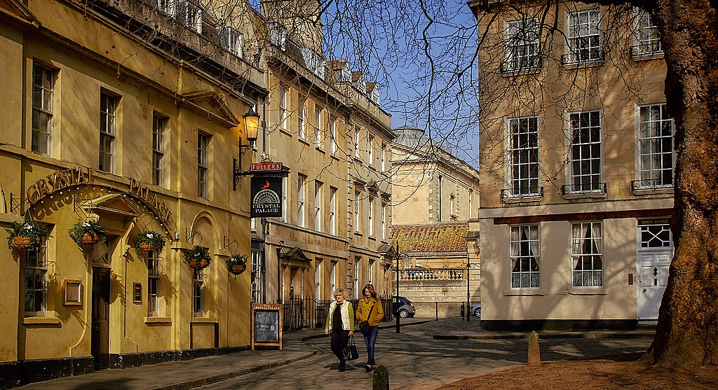 Edifícios de tons amarelos e bege em Bath, com duas mulheres a caminhar na rua