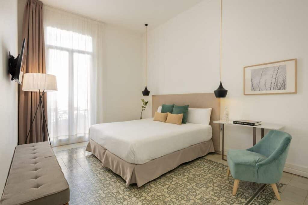 Quarto do Forget Me Not Barcelona, com lençóis brancos, almofadas amarelas e verdes e candeeiros suspensos de cada lado da cama.