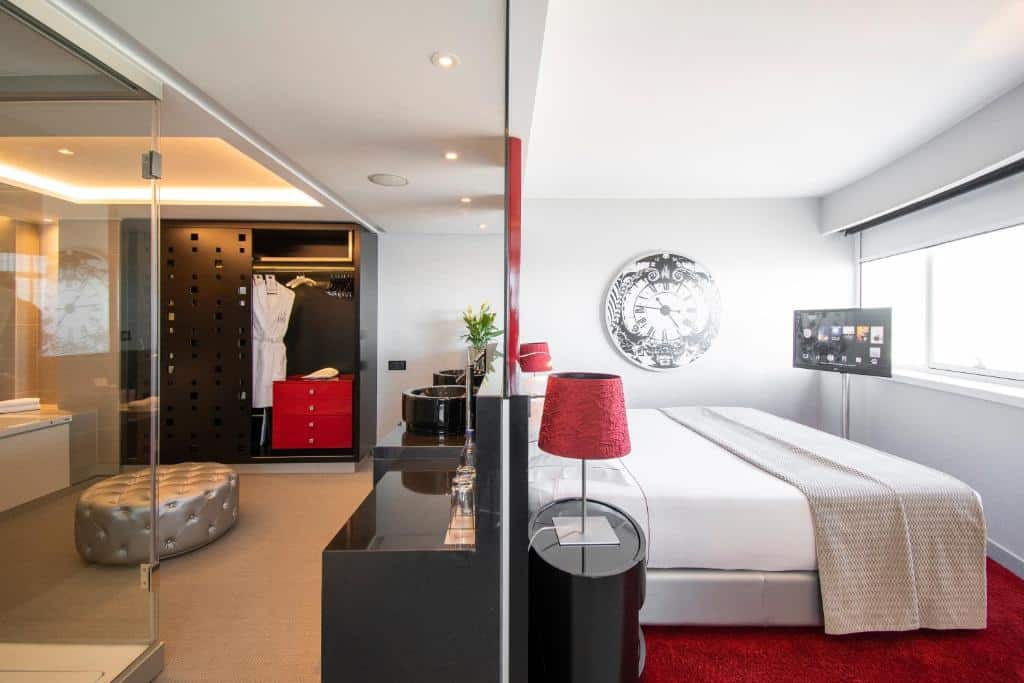 Quarto do MYRIAD by SANA Hotels com uma cama de casal virada para uma ampla janela onde há também uma televisão, e atrás da cama uma divisória com closet e aparador