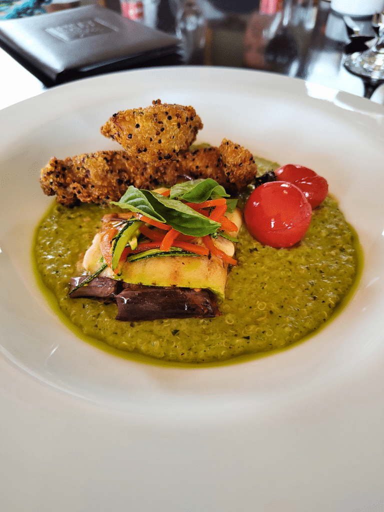 Prato branco com sopa de quinoa, legumes assados, tomate-cereja e frango panado, num restaurante em Maras
