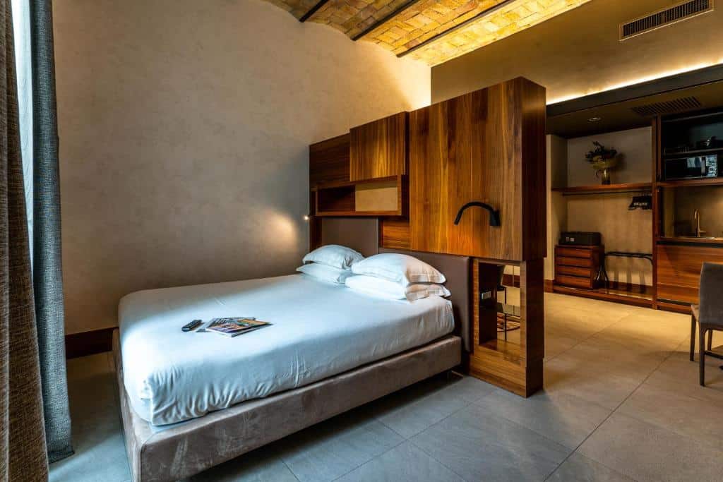 o Gasometer Urban Suites, um alojamento de férias em Roma, com cama de casal com uma divisória atrás que serve de guarda-roupa moderno, uma sala de estar ao fundo com móveis de madeira e uma janela em frente à cama