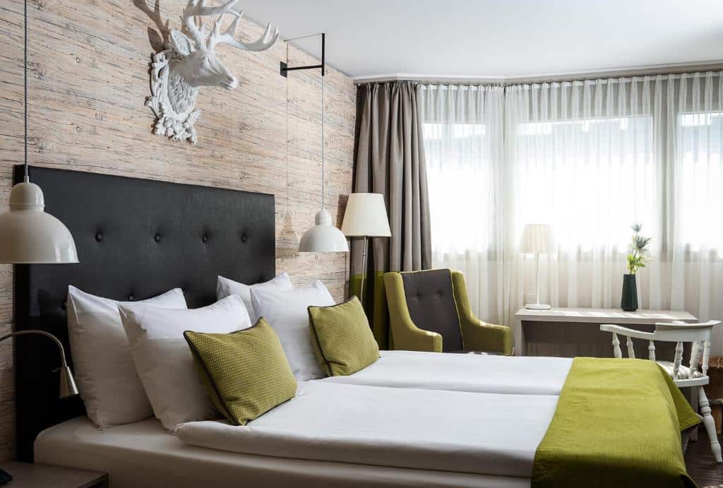 Quarto do AMERON Luzern, com cama de casal, candeeiros de teto laterais e secretária branca.