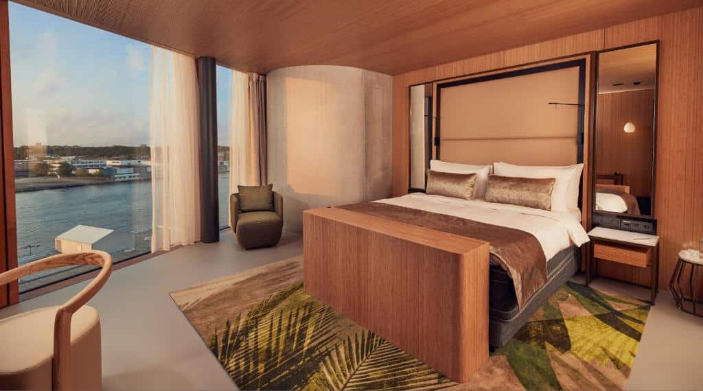 Suíte Junior do Hotel Jakarta, de 32 m², com cama de casal, mesinhas com espelho de cada lado, tapete decorado e parede de vidro com vista para um lago