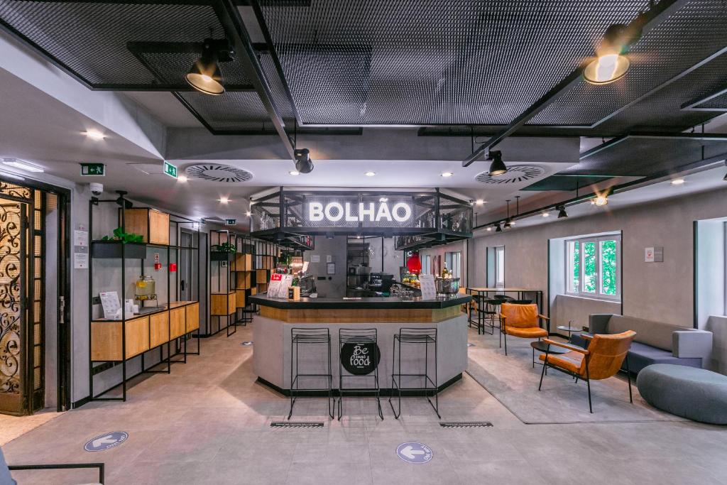 Interior de cafetaria moderna com um balcão central chamado "Bolhão", rodeado de lugares sentados e prateleiras, no ibis Porto Centro Mercado Bolhão.
