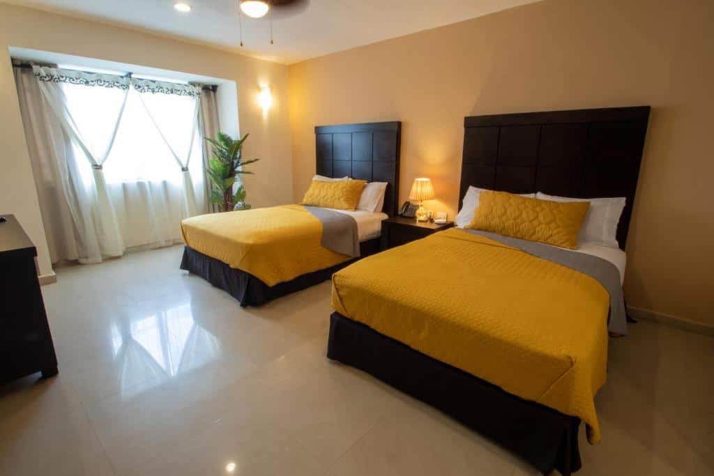 Quarto do Hotel Villas Segovia Playa del Carmen com duas camas de casal, roupa de cama amarela e cabeceiras escuras.