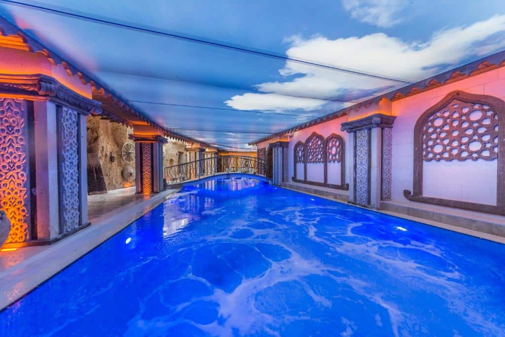 Piscina interior do Kapadokya Hill Hotel & Spa com paredes estampadas, janelas em arco e tecto pintado com céu azul e nuvens.