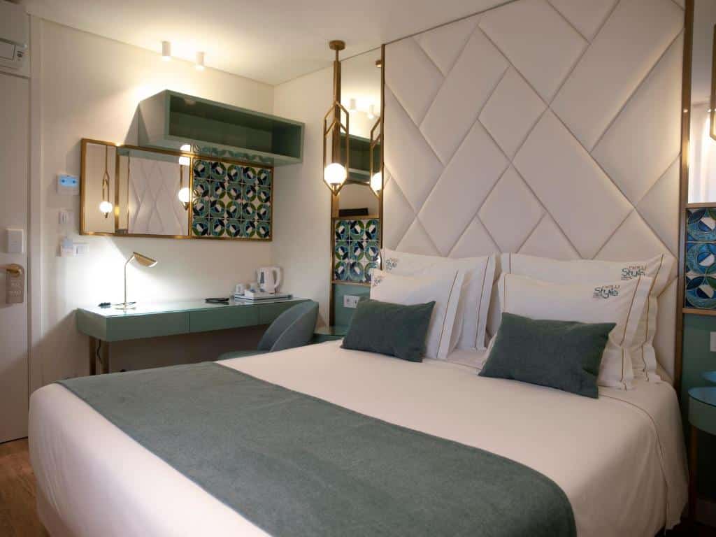 Quarto do New Style Lisbon Hotel com uma cama de casal de cabeceira estofada com pequenos espelhos nas laterais e, do lado esquerdo, uma secretária com cadeira.