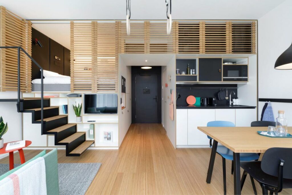 Vista geral do loft do hotel Zoku Copenhagen, com armários de cozinha, mesa de refeições, cadeiras e utensílios. Vê-se também uma escada que leva ao quarto.
