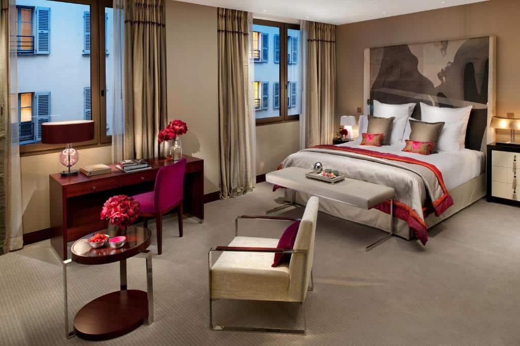 Quarto do Mandarin Oriental, Paris com uma cama de casal, secretária, cadeira, janelas com cortinas e detalhes decorativos em vermelho.