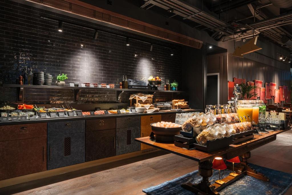 Um bufete com vários alimentos, frascos de vidro, fruta fresca e dispensadores de sumo num ambiente de restaurante moderno, na propriedade do Ruby Stella Hotel London.