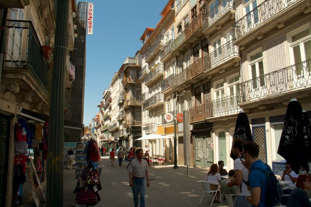 Rua das Flores durante o dia, com pessoas a caminhar e casas antigas ao fundo, à direita.