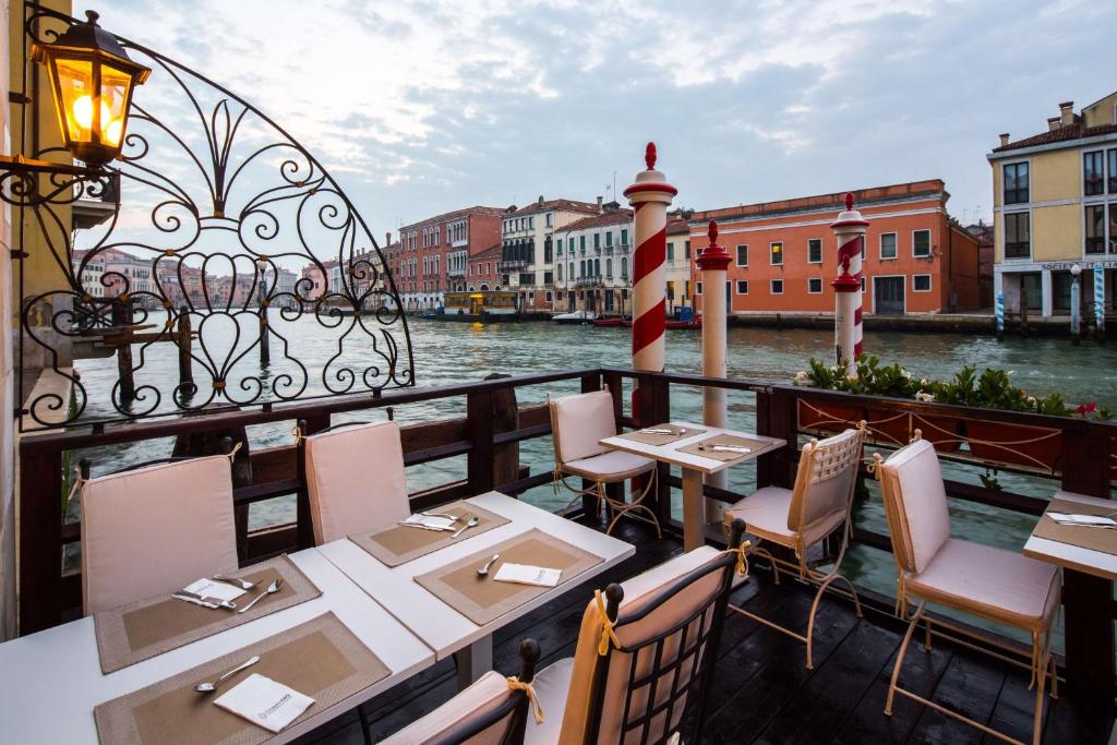 Terraço com vista para o canal em Veneza, Itália, com mesas e cadeiras de um restaurante ao ar livre e elementos em ferro forjado