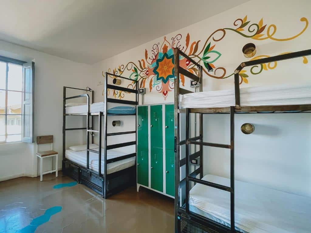 Quarto do Madama Hostel &amp; Bistrot com dois beliches pretos e, entre eles, um armário com fechaduras; as paredes estão pintadas com flores coloridas e há uma janela no espaço