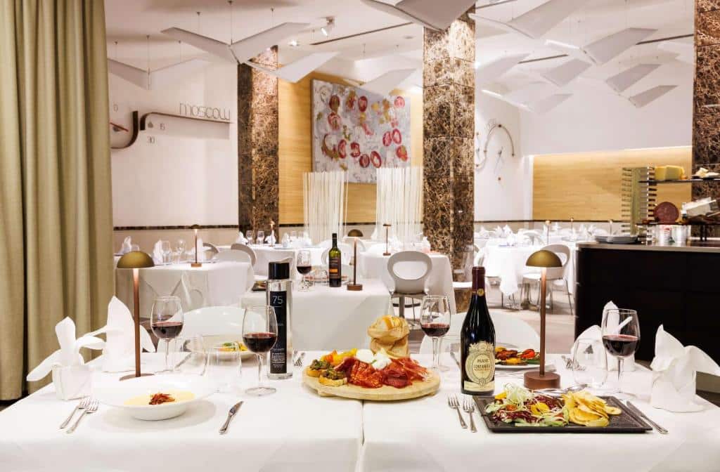 sala do Best Western Premier Hotel Royal Santina, uma das opções de onde ficar em Roma, com toalhas brancas, cadeiras confortáveis, quadros na parede e colunas trabalhadas, com vinhos e enchidos servidos na mesa