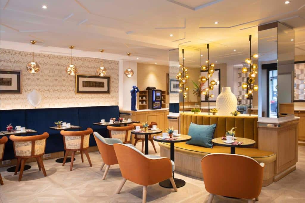 Cafetaria moderna do Philéas Lazare & Spa com mesas redondas, cadeiras laranja e candeeiros suspensos num espaço bem iluminado.