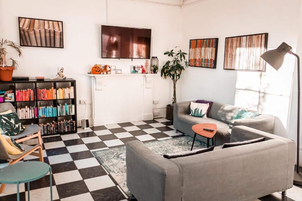 Sala partilhada do Urbany Hostel London com dois sofás, cadeiras, uma televisão, alguns quadros e candeeiros, além de uma estante cheia de livros.