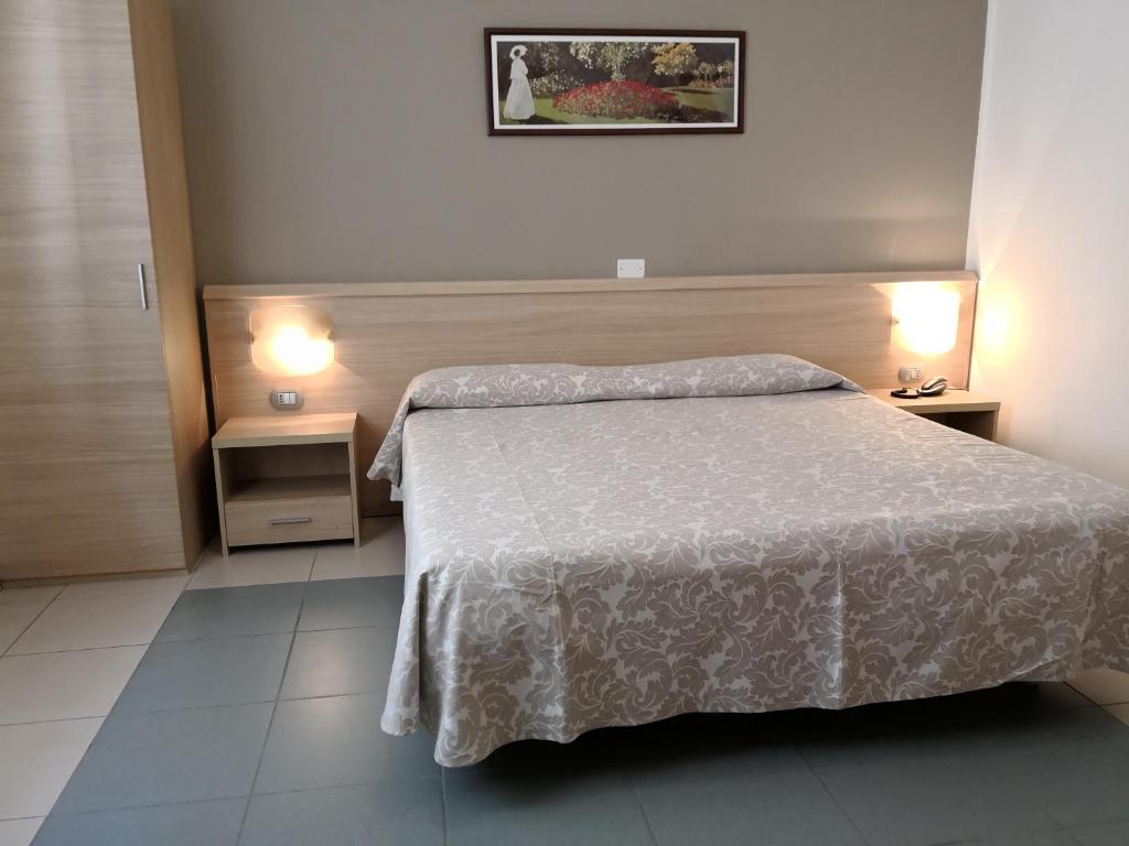 Quarto de hotel moderno com decoração leve, cama de casal com edredão de padrão floral, mesa de cabeceira com candeeiro e um quadro decorativo na parede