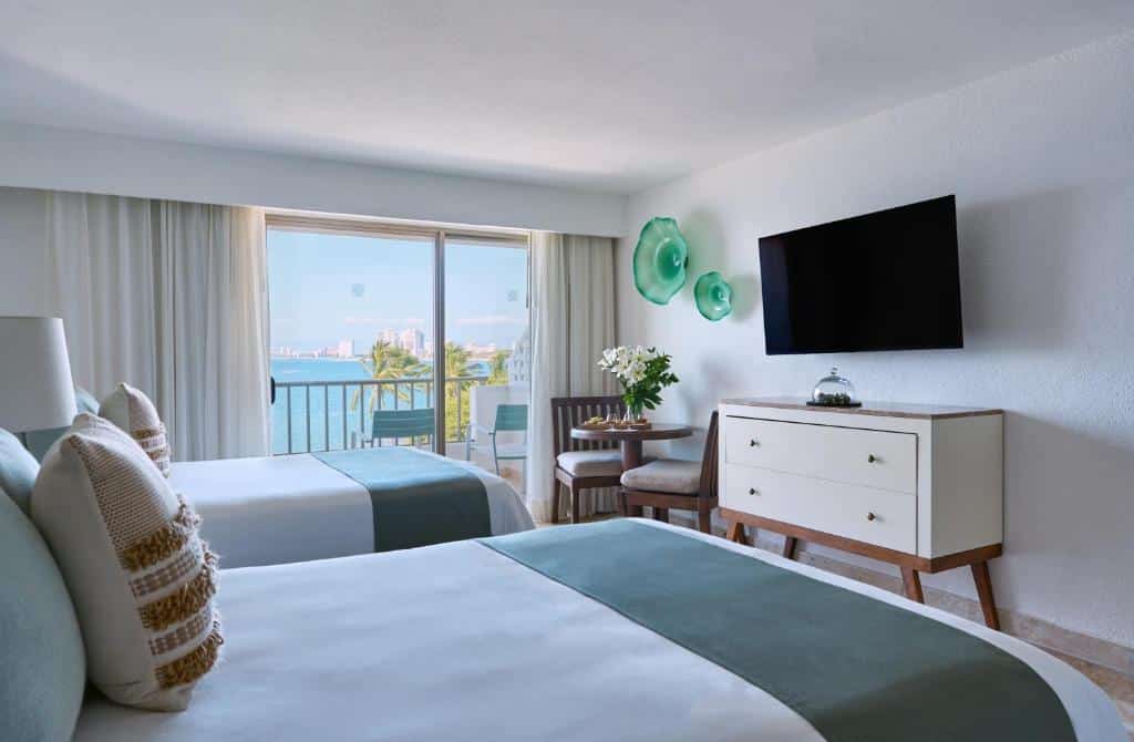 Quarto do Villa Premiere Boutique Hotel com duas camas, uma TV na parede, uma cómoda, cadeiras junto a uma mesa e uma varanda com vista para o mar.